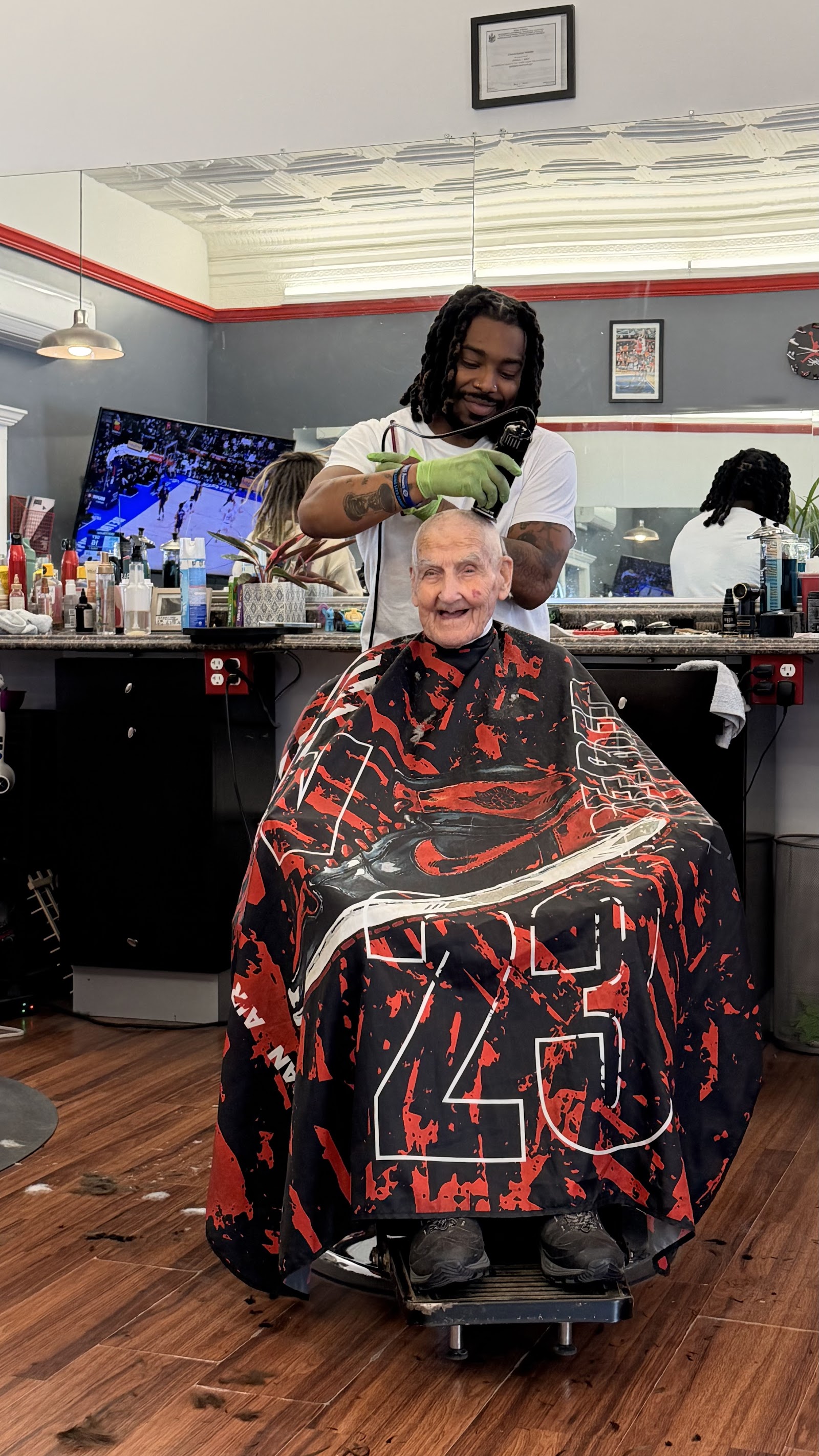 A barber in gloves clippering an older gentleman’s hair while he smiles in the chair.